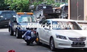 Petugas Dishubkominfo sedang menggembok ban mobil warga yang parkir sembarangan.