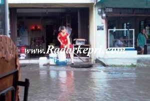 Seorang warga Jl Tambak sedang menghalangi air masuk ke tokonya.